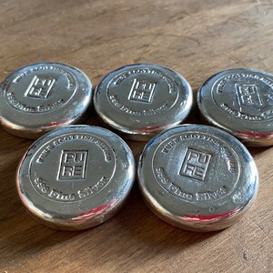 Puede incluir: Cinco barras de plata con las palabras "Pure Scottish Silver 999 Fine Silver" y un logotipo de un cuadrado con las letras "PU" en su interior.