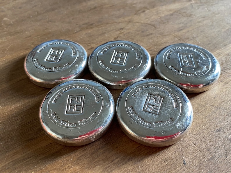 Puede incluir: Cinco barras de plata con las palabras "Pure Scottish Silver 999 Fine Silver" y un logotipo de un cuadrado con las letras "PU" en su interior.