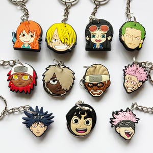 May include: A selection of anime character keyrings. Each keyring showcases a colourful, detailed character head made of rubber, attached to a silver metal ring. The characters have unique hairstyles and facial expressions.
