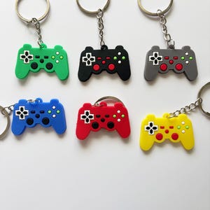 以下が含まれることがあります： 6つのカラフルなゲームコントローラーキーホルダー。キーホルダーは緑、黒、グレー、青、赤、黄色の6色。各コントローラーにはシルバーのキーリングとチェーンが付いています。コントローラーには黒、赤、緑のボタンが付いています。