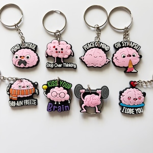 Può includere: Una collezione di portachiavi originali con ciondoli a forma di cervello rosa. Ogni ciondolo ha un'espressione e una frase diversa, come "Mind Control" e "Oh Synapse!". Ogni portachiavi ha un anello e una catena argentati.