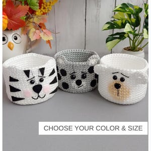 May include: Three round crochet baskets featuring animal faces. The left basket is white with black stripes and pink cheeks. The middle basket is grey with black spots. The right basket is white with a tan muzzle. Text reads: CHOOSE YOUR COLOR & SIZE.