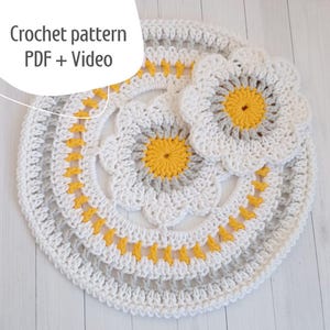 May include: Crochet pattern PDF + Video. A set of three crocheted white and grey coasters with yellow centres. The coasters are in the shape of a flower.