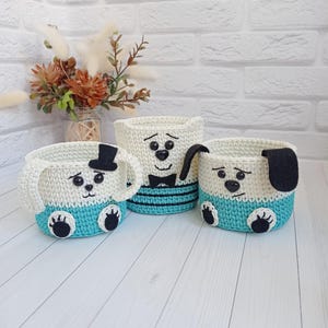 Peut inclure: Trois paniers crochetés faits à la main en forme de chiens. Les paniers sont blancs et turquoise, avec des détails noirs pour les yeux, le nez et les pattes. L'un a un chapeau haut de forme noir, un autre un nœud papillon et le troisième une oreille noire.