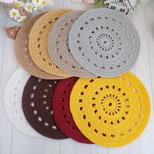 May include: A set of seven crocheted doilies in various colors, including white, brown, red, yellow, beige, and gray. The doilies are arranged in a circle, with the largest doily in the center and the smallest doily on the outside.
