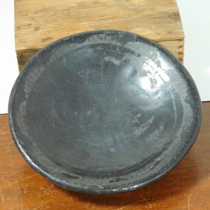 May include: A black ceramic bowl with a smooth, glossy finish. The bowl is slightly curved and has a wide, shallow opening.