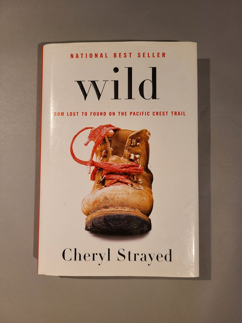 May include: A book cover with the title "wild" in bold, black font. The subtitle is "From Lost to Found on the Pacific Crest Trail". The cover features a close-up of a brown hiking boot with red laces. The author's name, "Cheryl Strayed", is printed in black at the bottom of the cover.