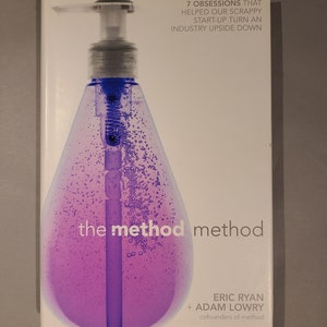 May include: A book titled "The Method Method" by Eric Ryan and Adam Lowry, co-founders of Method. The book cover features a purple and clear soap bottle with a pump dispenser. The text on the cover reads "7 Obsessions That Helped Our Scrappy Start-Up Turn An Industry Upside Down."