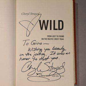 May include: A signed copy of the book "Wild: From Lost to Found on the Pacific Crest Trail" by Cheryl Strayed. The inscription reads "To Gina - Wishing you beauty on the journey. It was an honor to meet you."