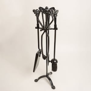 Puede incluir: Un juego de herramientas para chimenea negro con un soporte. El juego incluye un atizador, una pala, unas tenazas y un cepillo. El soporte tiene un diseño decorativo en la parte superior y una base de tres patas. Las herramientas son de metal.