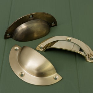 Peut inclure: Trois poignées de tiroir en laiton antique, deux sont en forme de coupe et une est une simple poignée incurvée.