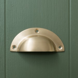 May include: A brass cup-shaped cabinet pull with a rounded edge and four screw holes.