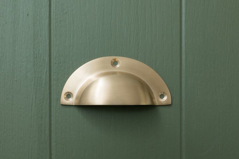 May include: A brass cup-shaped cabinet pull with a rounded edge and four screw holes.