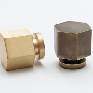 May include: Two hexagonal cabinet knobs, one in polished brass and one in aged brass. Both knobs have a round base.