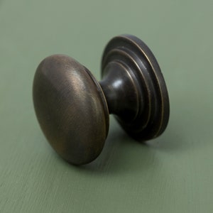 May include: A round, antique brass cabinet knob with a fluted base. The knob has a smooth, slightly textured surface.
