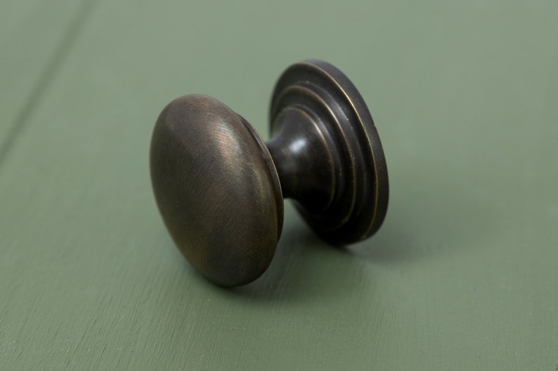 May include: A round, antique brass cabinet knob with a fluted base. The knob has a smooth, slightly textured surface.