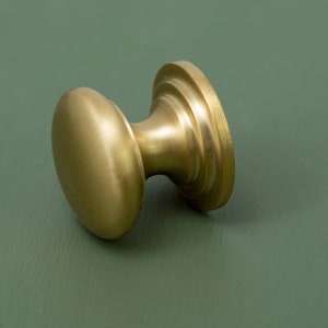 May include: A gold-toned cabinet knob with a round, slightly domed top and a fluted base.