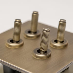 May include: A brass light switch plate with four toggle switches. Each switch has a round knob with a fluted, cylindrical handle.