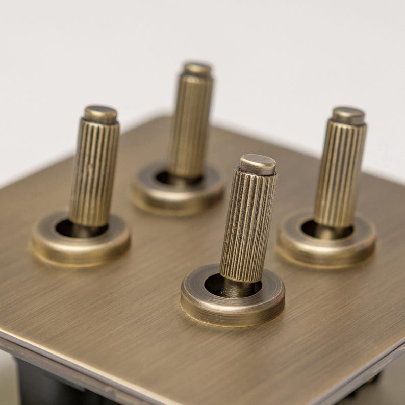 May include: A brass light switch plate with four toggle switches. Each switch has a round knob with a fluted, cylindrical handle.