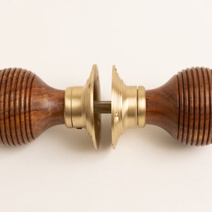 Peut inclure: Une paire de boutons de porte en bois avec un centre en laiton. Les boutons sont de couleur brun foncé et ont une texture côtelée.