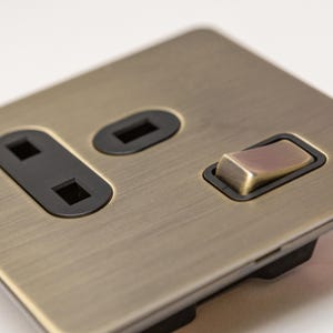 May include: A brushed antique brass electrical outlet with a single switch. The outlet has a black plastic surround and the switch has a brass toggle.