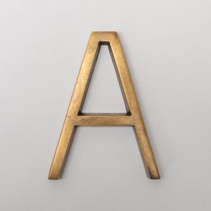 May include: A capital letter A in a sans-serif font, constructed from a metallic material with a brushed, antique brass finish. The letter features a three-dimensional structure with visible depth and a consistent, smooth, golden-brown surface texture.