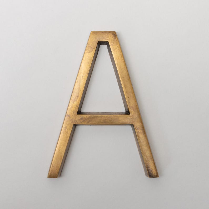 May include: A capital letter A in a sans-serif font, constructed from a metallic material with a brushed, antique brass finish. The letter features a three-dimensional structure with visible depth and a consistent, smooth, golden-brown surface texture.