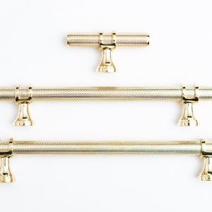 May include: Three gold cabinet pulls with a textured finish. The pulls have a simple, elegant design with a rounded shape.