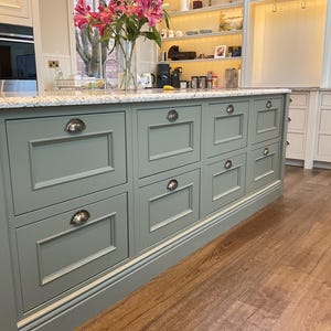 May include: A kitchen island with a light green painted finish and multiple drawers with silver handles. The island has a granite countertop and sits on a wood floor.
