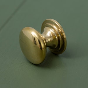 May include: A polished brass door knob with a round, slightly domed shape and a decorative ring around the base.