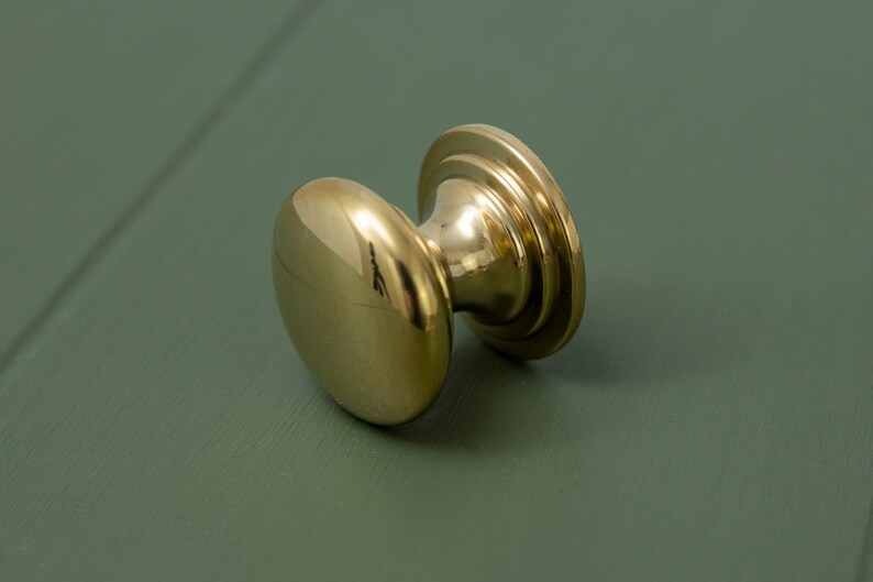 May include: A polished brass door knob with a round, slightly domed shape and a decorative ring around the base.
