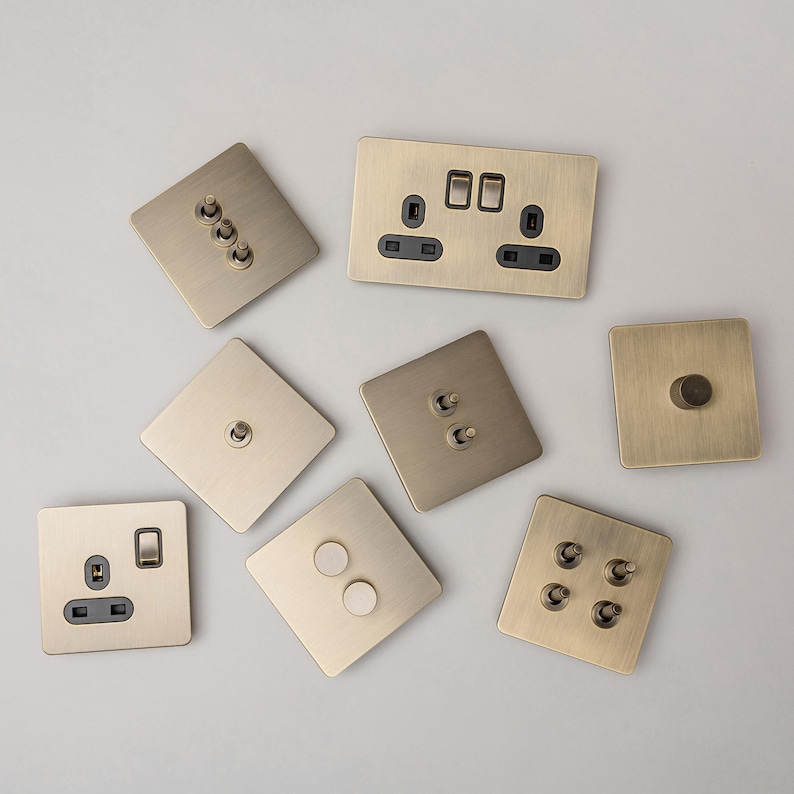May include: A collection of eight brass light switch plates and electrical outlets. The plates are in various configurations, including single, double, and triple switches, as well as a single outlet. The plates are all made of a brushed brass finish.