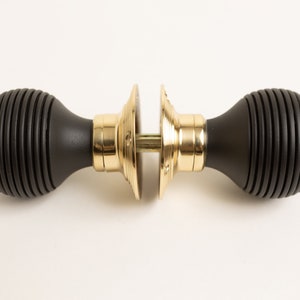 Może przedstawiać: Czarny gałka drzwiowa z żebrowanym wzorem i złotą metalową podstawą.