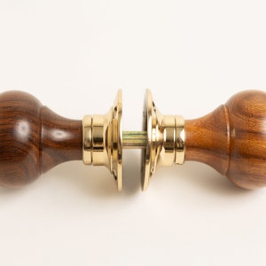 Może przedstawiać: Para drewnianych gałek drzwiowych z mosiężnymi akcentami. Gałki są okrągłe i mają gładkie, polerowane wykończenie.