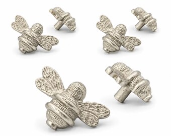 May include: A set of six silver-toned metal cabinet knobs shaped like bees. Each knob features a textured body and wings with a metallic finish, designed with a central post for attachment to furniture drawers or cabinet doors for functional use.