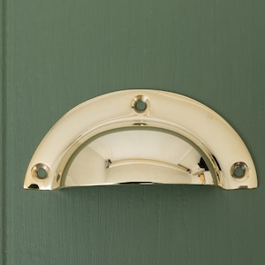 May include: A polished brass cabinet pull with a rounded, half-circle shape. The pull has three visible screw holes.