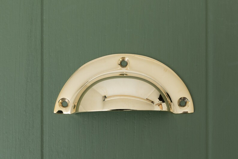 May include: A polished brass cabinet pull with a rounded, half-circle shape. The pull has three visible screw holes.