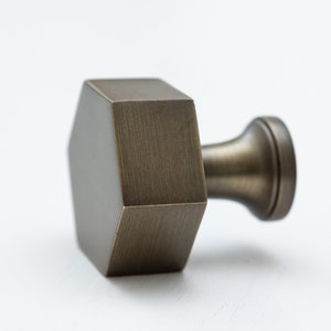 Puede incluir: Un pomo hexagonal de latón con acabado cepillado y base redonda. El pomo es una pieza de ferretería decorativa.