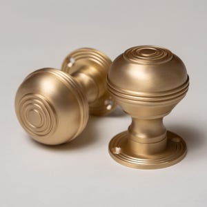 May include: Two gold door knobs with a circular design. The knobs have a smooth, brushed finish and are made of metal.