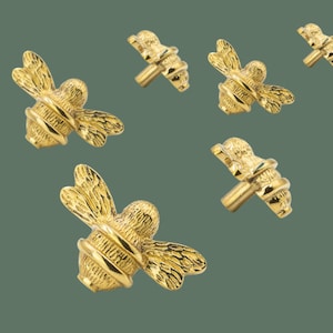 Könnte beinhalten: Sechs goldfarbene, bien detaillierte Bienen-Knöpfe mit einer strukturierten Oberfläche. Die Knöpfe haben Flügel, einen Stachel und einen runden Körper.