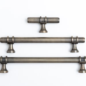 May include: Three antique brass cabinet pulls with a textured finish. The pulls are in different sizes, with the smallest pull at the top and the largest pull at the bottom.