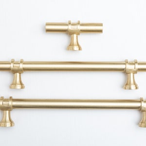 May include: Three gold-toned cabinet pulls with a simple, modern design. The pulls are made of metal and have a brushed finish. The smallest pull is about 3 inches long, the middle pull is about 6 inches long, and the largest pull is about 9 inches long.