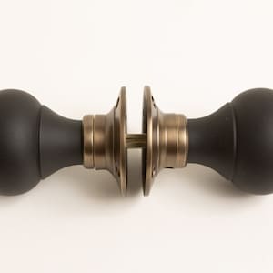 Può includere: Pomo per porta nero con finitura in ottone. Il pomo è rotondo e ha una superficie liscia.