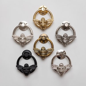 Può includere: Sei battenti per porta circolari con un design centrale a forma di ape. La collezione include finiture in oro lucido, argento spazzolato, ottone antico, nero opaco, cromo lucido e una tonalità metallica scura, ciascuno con piastra di montaggio.