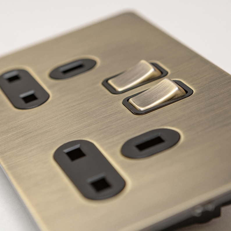 May include: A brushed brass electrical outlet cover with two toggle switches and two standard outlets. The cover has a brushed finish and is designed for a modern aesthetic.