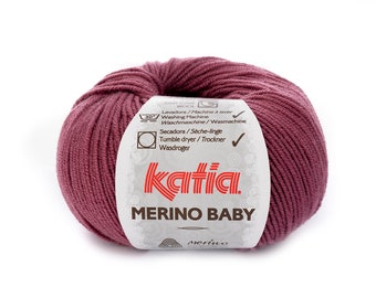 May include: A ball of deep mauve yarn with a white paper label featuring the red text Katia and brown text Merino Baby. The label includes icons for machine washing at 30 degrees and tumble drying, along with the words Easy Care Wool.