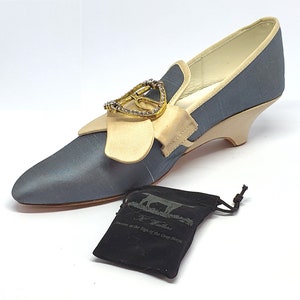 May include: A gray and beige satin shoe with a gold and crystal heart-shaped buckle. The shoe is on a white background and comes with a black velvet pouch that says "Jeweler of the Sign of the Gray Horse".