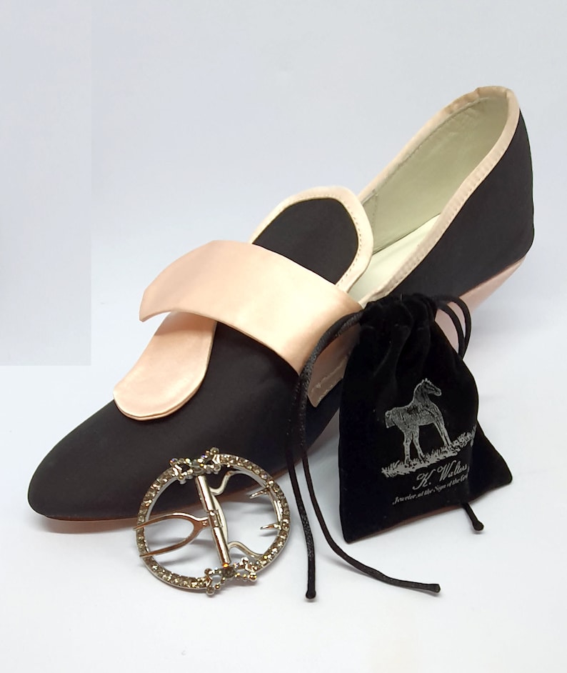 May include: A black satin shoe with a pink satin strap and buckle. The shoe has a small velvet bag with a horse design and the text "H. Walters, Jeweller at the Sign of the Bell" on it.