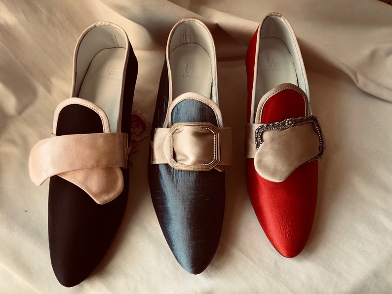 May include: Three pairs of pointed-toe shoes with decorative buckles. The shoes are black, blue, and red.