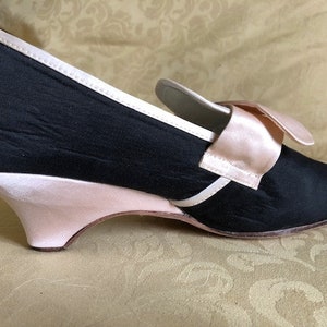 May include: Black satin heeled shoe with a pink satin bow and trim. The heel is a pink wedge.